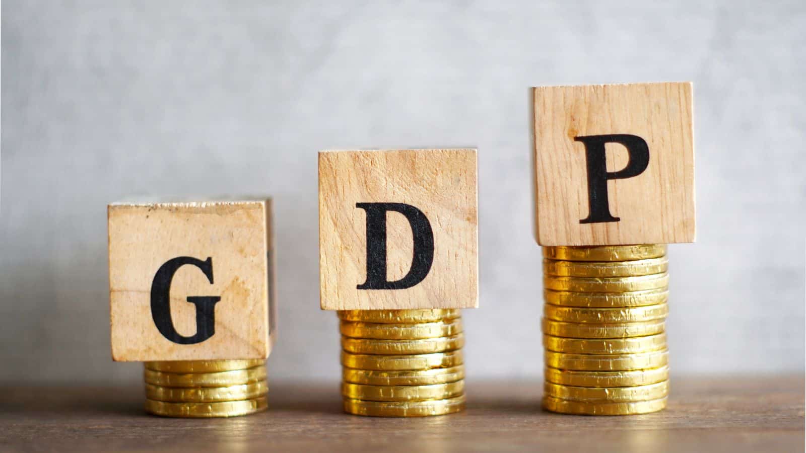 Wooden blocks with letters G, D, P on stacked coins representing economic growth and oil price effects.