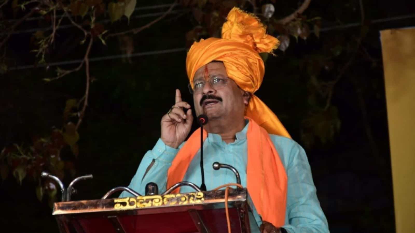 Traditional Indian man with orange turban speaking into microphone during an outdoor event.