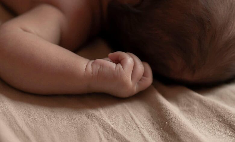 Close-up of a sleeping newborn baby with tiny hand curled near face.
