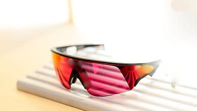 Sunglasses with red and black frame and mirrored pink lenses resting on a wooden slatted surface.