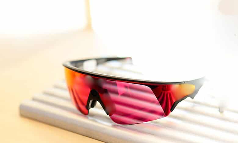 Sunglasses with red and black frame and mirrored pink lenses resting on a wooden slatted surface.