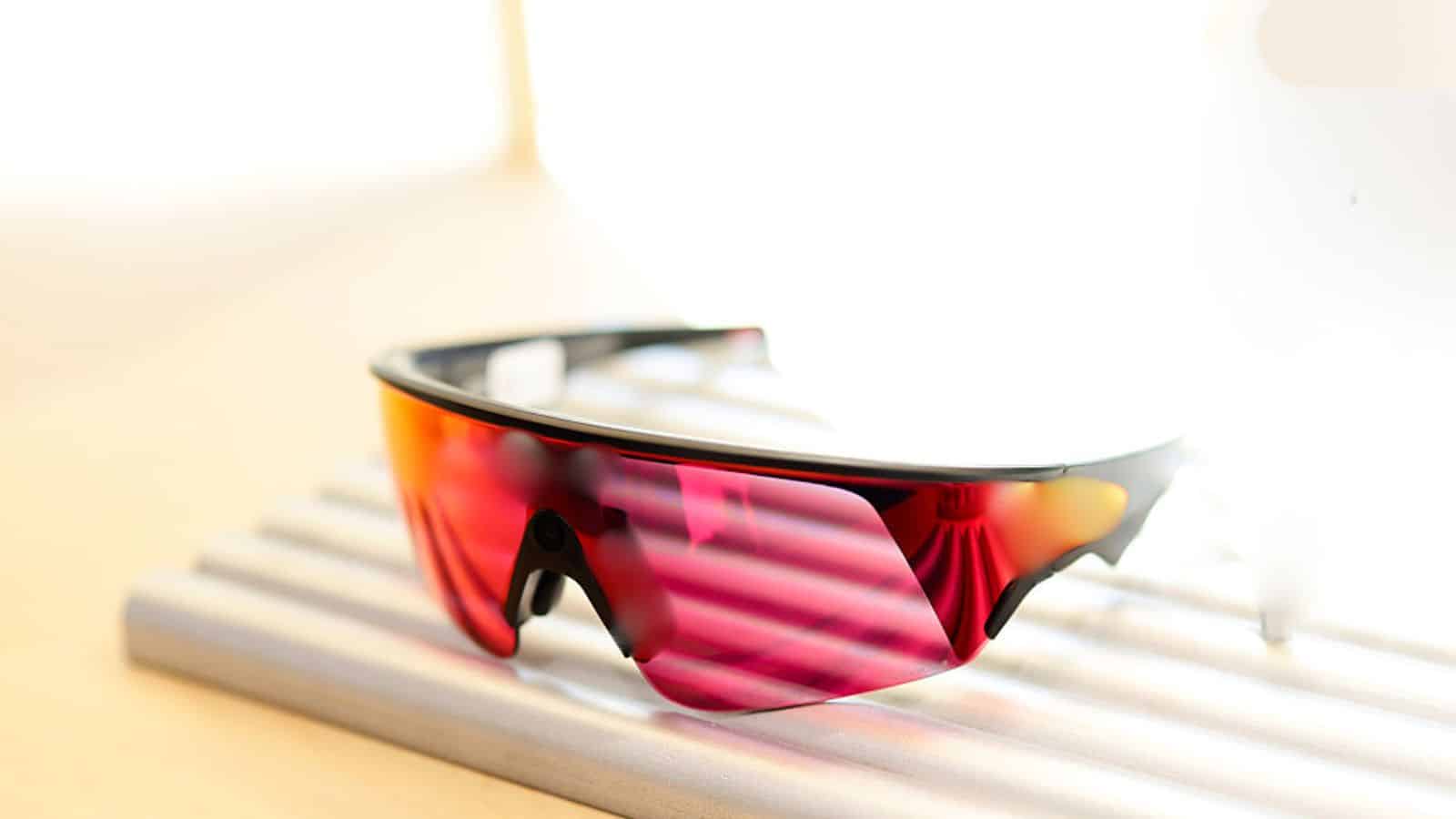 Sunglasses with red and black frame and mirrored pink lenses resting on a wooden slatted surface.