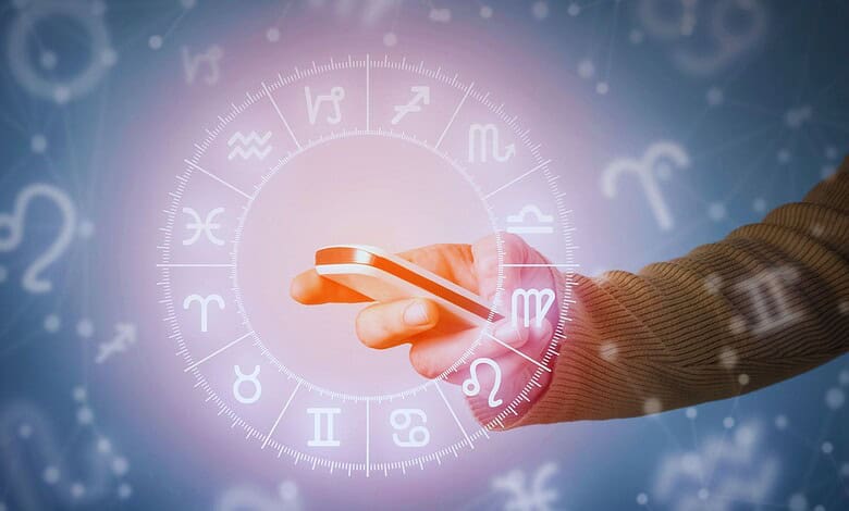 Hand holding smartphone with zodiac wheel and astrological symbols in the background.