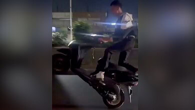 A man riding a black scooter at night on a city street.