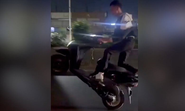 A man riding a black scooter at night on a city street.