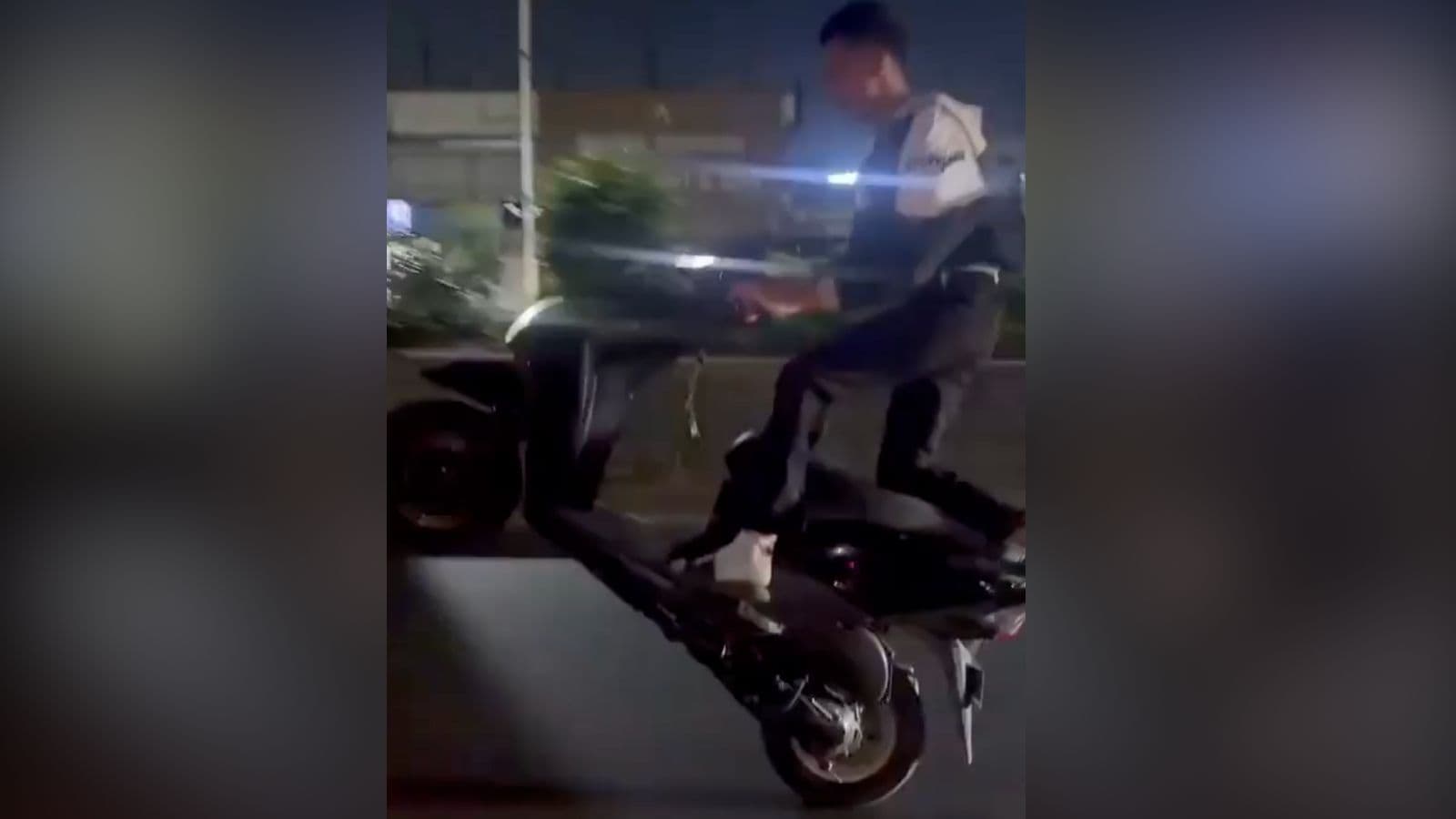 A man riding a black scooter at night on a city street.