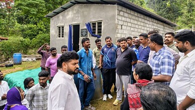 Community members and leaders engaged in discussion outside a modest rural home.