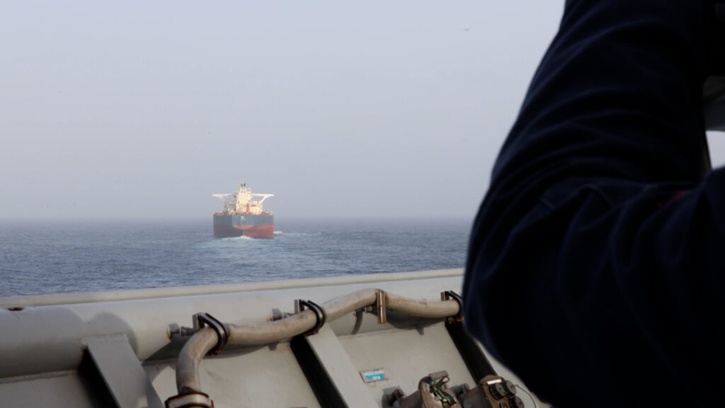 Oil tanker sailing in open sea with a person on a ship deck in the foreground.
