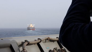Oil tanker sailing in open sea with a person on a ship deck in the foreground.