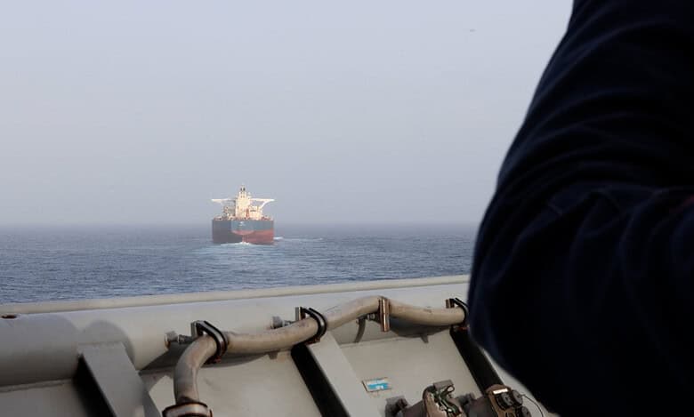 Oil tanker sailing in open sea with a person on a ship deck in the foreground.