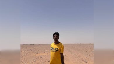 Young man standing in a vast, arid desert landscape under a clear blue sky.