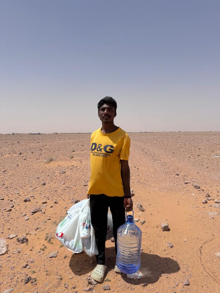 Dasari Aravind stands in a remote desert area in Saudi Arabia holding grocery bags and a water container provided by volunteers.
