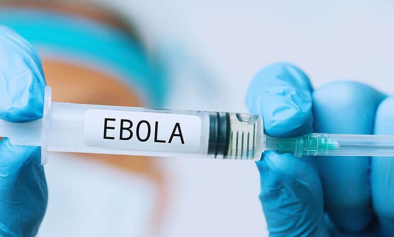 A healthcare professional in blue gloves holding a syringe labeled 'Ebola' vaccine, highlighting efforts to combat Ebola outbreaks.