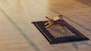 Prayer rug with Quran and prayer beads placed on wooden floor, symbolising Islamic worship and spirituali.