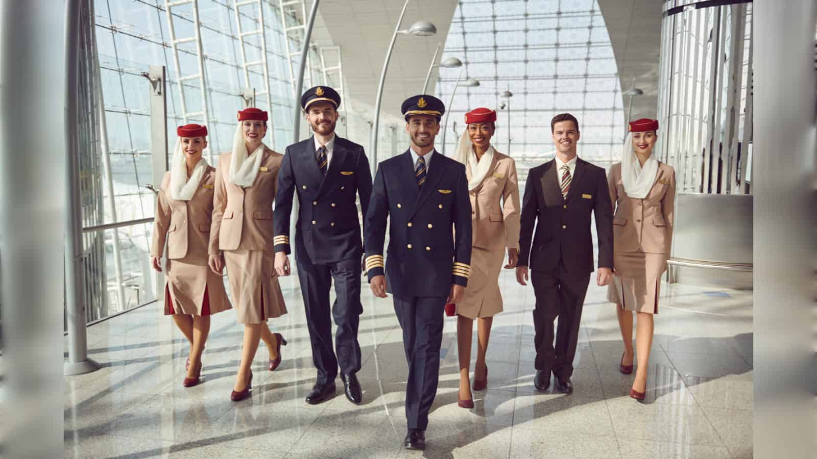 Emirates pilots and cabin crew walk through an airport terminal in official airline uniform.