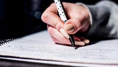 A person writing in a notebook with a pen, close-up shot.