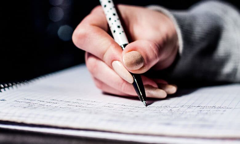 A person writing in a notebook with a pen, close-up shot.