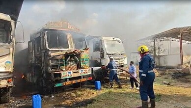 Burnt vehicles after fire in open field used for parking in Hyderabad, with firefighters working to contr.