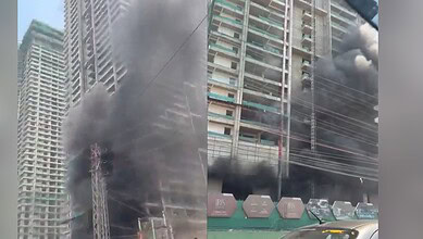 Fire incident at high-rise building with thick black smoke and flames, urban area with construction and v.