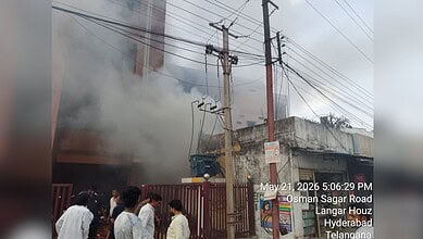 A fire incident at Osman Sagar Road, Hyderabad, with smoke billowing from a building and people observing.