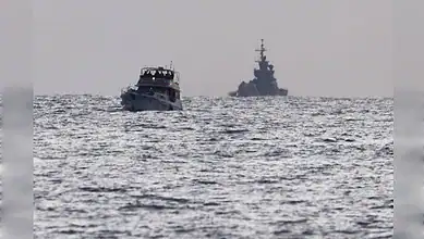 A small boat and a large warship sailing on open water under a cloudy sky.