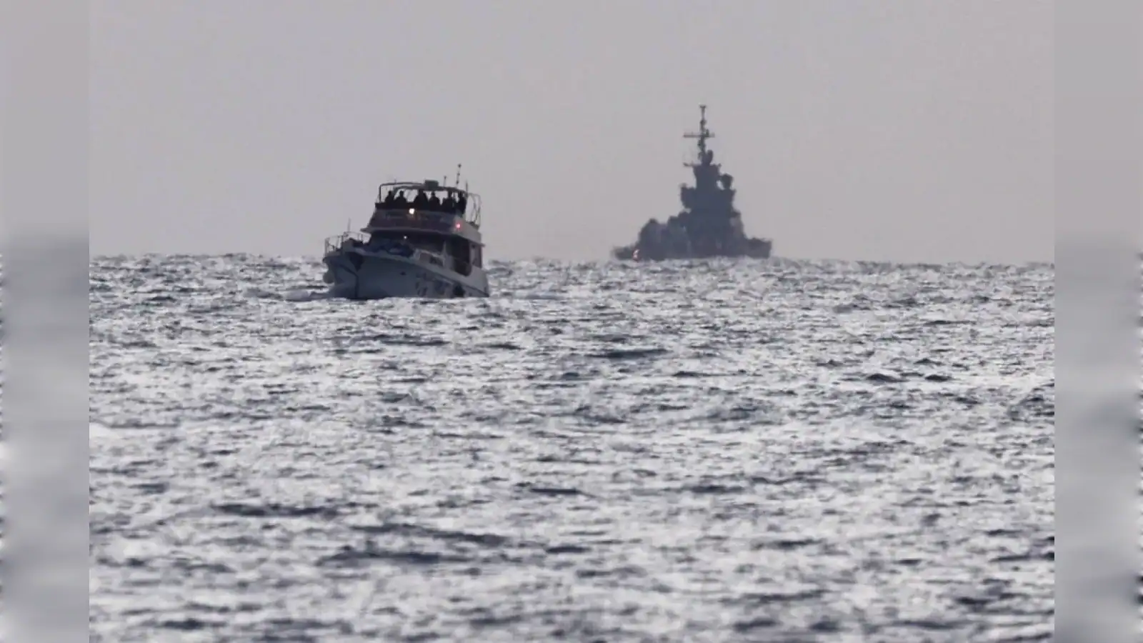 A small boat and a large warship sailing on open water under a cloudy sky.