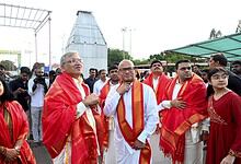 Celebration event with dignitaries and attendees wearing traditional red shawls at an outdoor gathering.