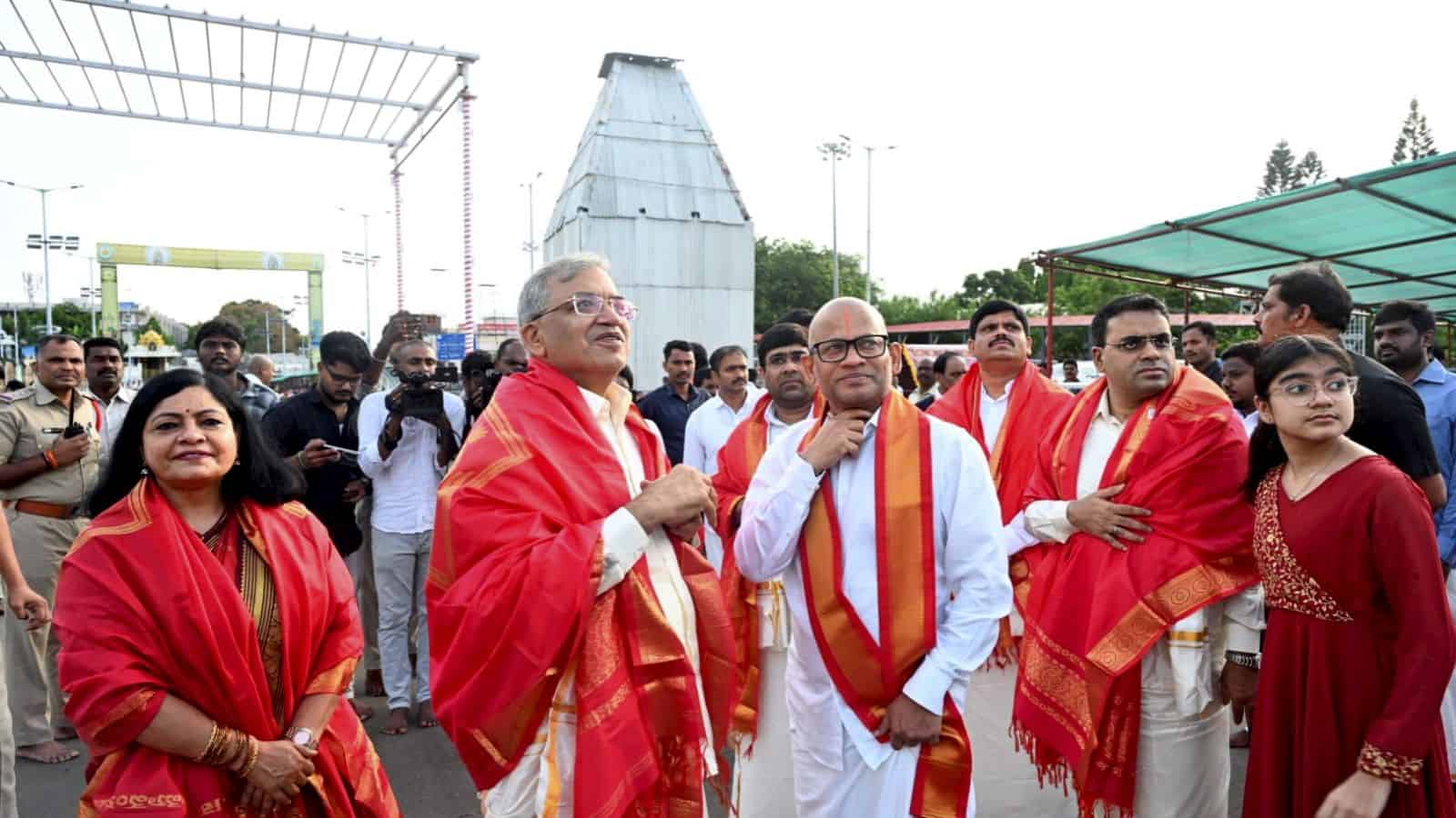 Celebration event with dignitaries and attendees wearing traditional red shawls at an outdoor gathering.