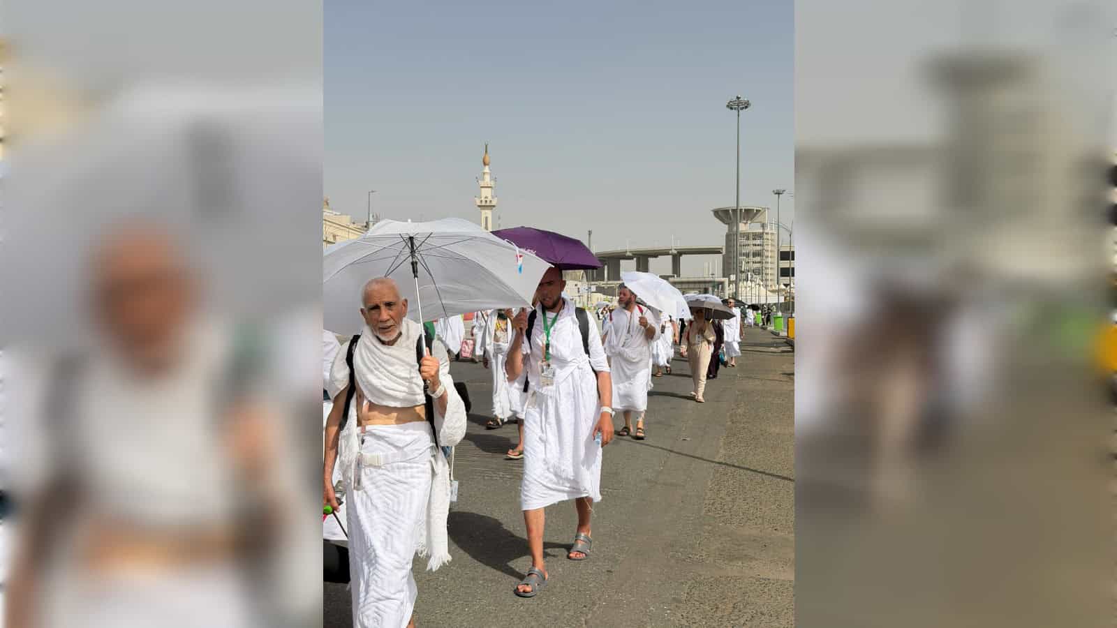 Pilgrims walking with umbrellas during Hajj pilgrimage in Mecca, Saudi Arabia, with modern buildings and.