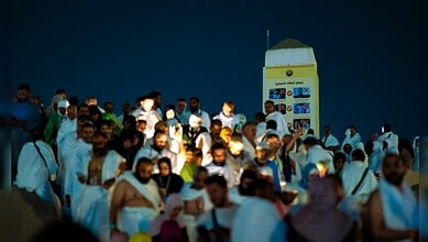 Crowd of men and women dressed in white attending a religious gathering outdoors at night.