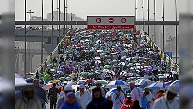 Crowd of people with umbrellas at a busy border crossing, under a "No Way Up" sign, during rainy weather.