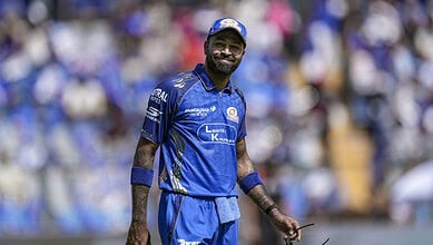 A cricket player in blue uniform smiling on the field during a match.