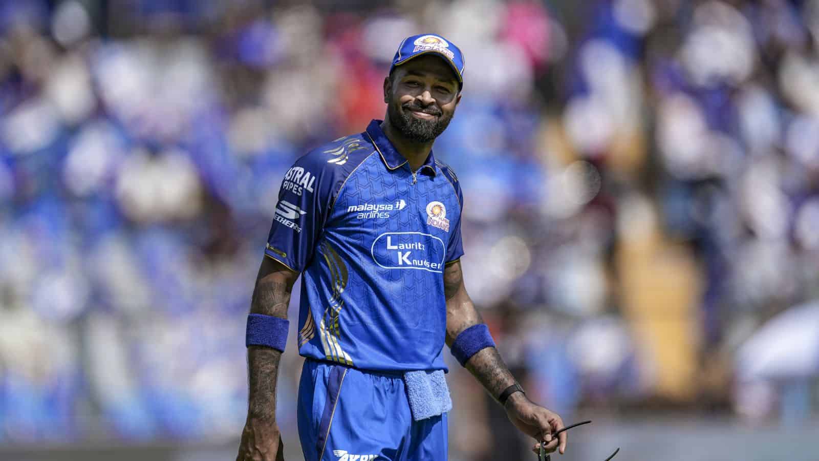A cricket player in blue uniform smiling on the field during a match.