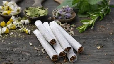 Hand-rolled herbal cigarettes with dried herbs and flowers on rustic wooden surface, natural alternative.