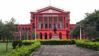 Elegant red courthouse building with classical architecture and a statue in front, surrounded by greenery.