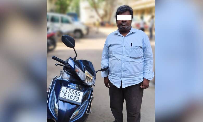 Man standing next to a scooter with a fake number plate in Hyderabad, police arresting suspect for using.