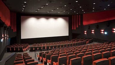 A nearly empty movie theatre with a large blank screen and rows of red and black seats.