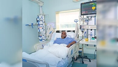 Patient in hospital bed with monitoring equipment and medical staff support.
