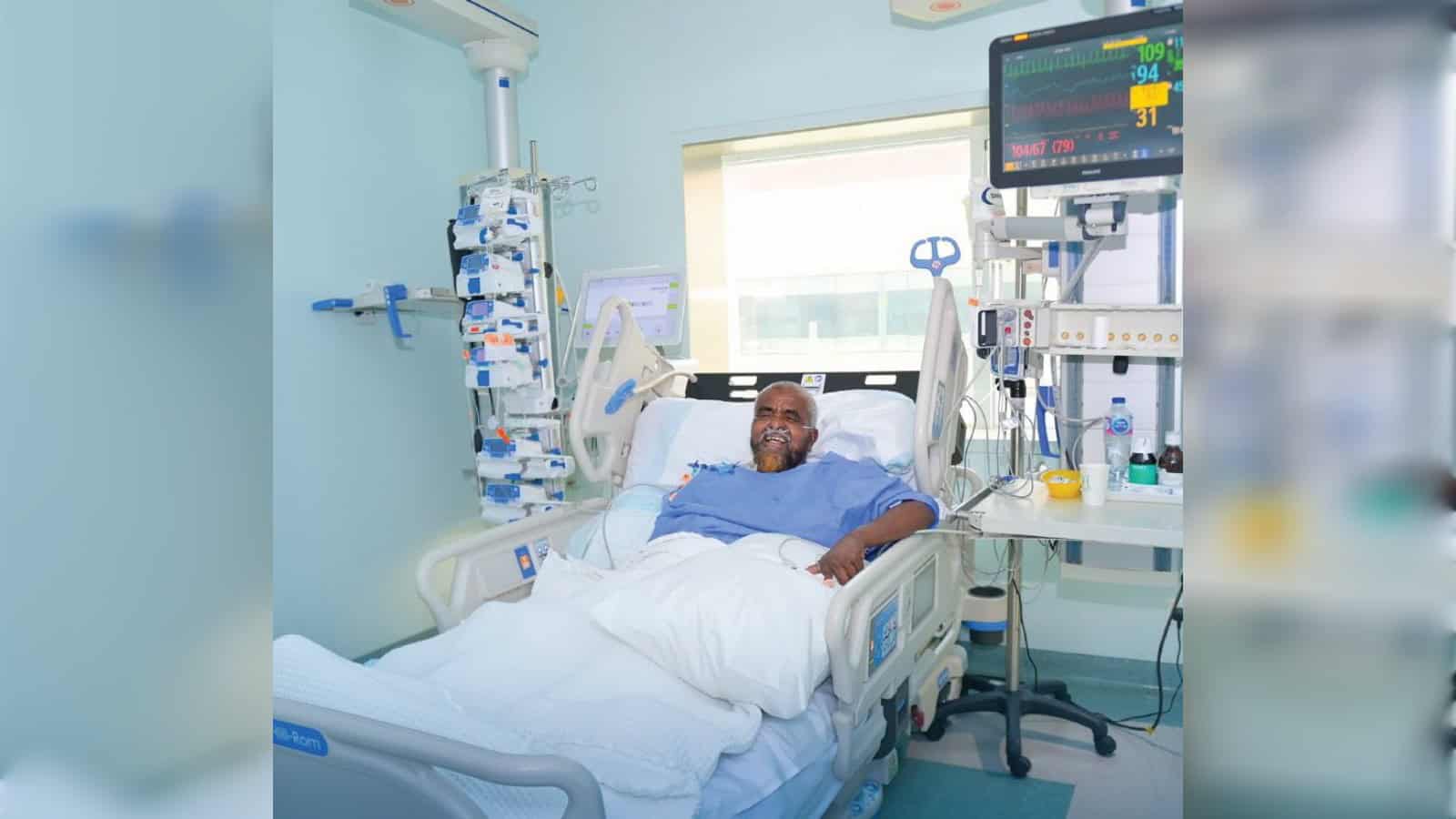 Patient in hospital bed with monitoring equipment and medical staff support.