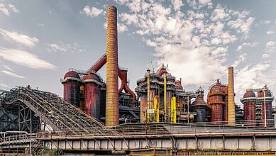 Industrial factory with large chimneys and complex piping under a partly cloudy sky.
