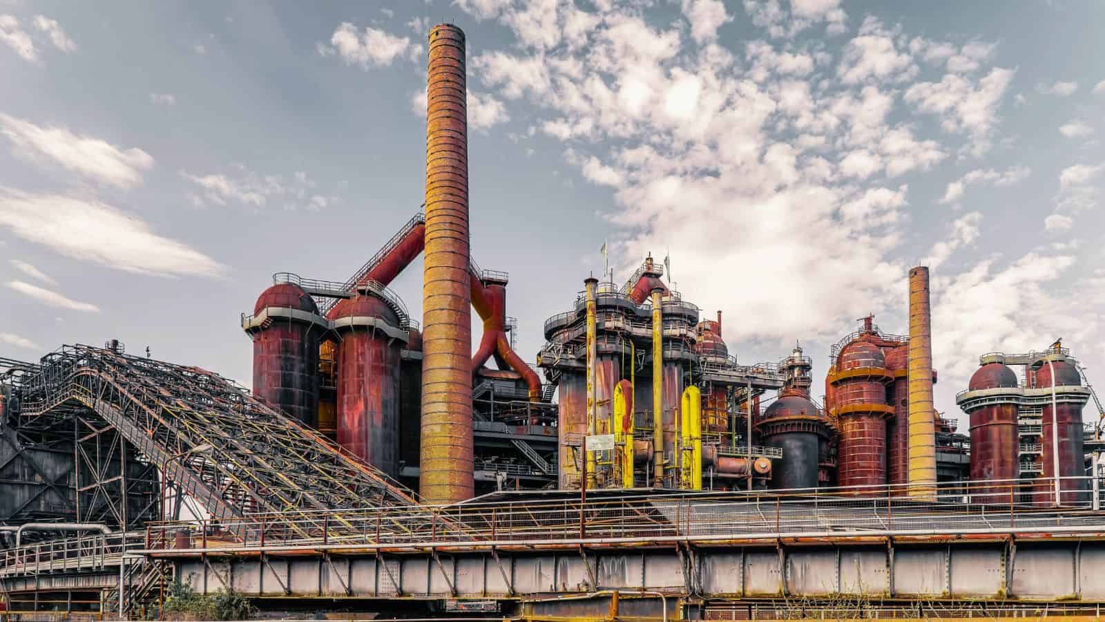 Industrial factory with large chimneys and complex piping under a partly cloudy sky.