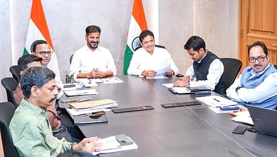 India government officials in a meeting with Indian flags in the background.