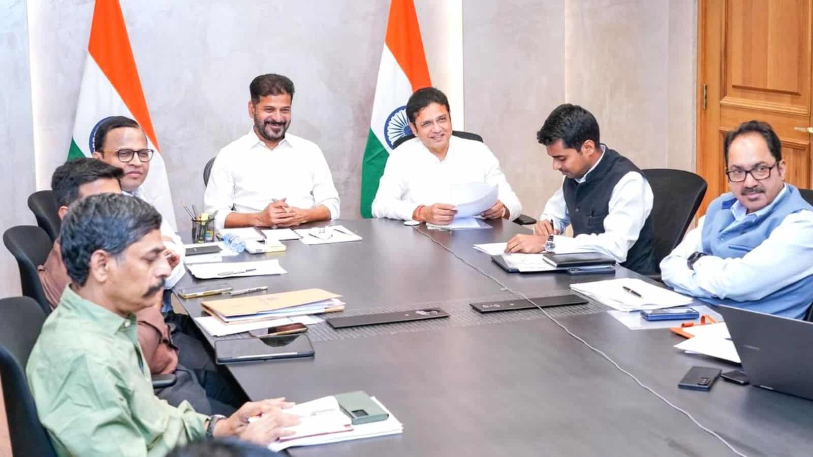 India government officials in a meeting with Indian flags in the background.