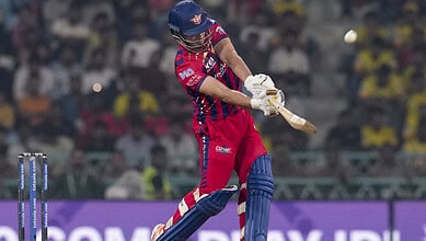 A young cricket player in red and blue uniform hitting the ball during a match.