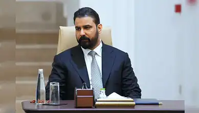 Businessman in formal attire sitting at a desk in a professional office environment.