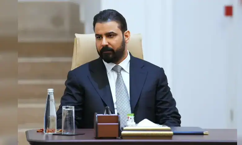 Businessman in formal attire sitting at a desk in a professional office environment.