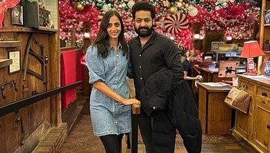 A young woman and a man smiling together in a festive, decorated store with Christmas ornaments and light.