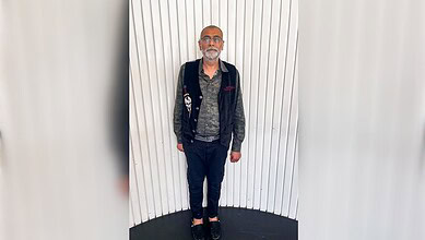 Kamlesh Parekh standing against a white panel wall after extradition.