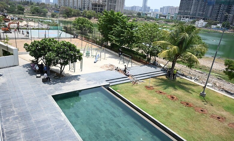 Swimming pool and green garden area in a modern residential complex with city skyline in the background.