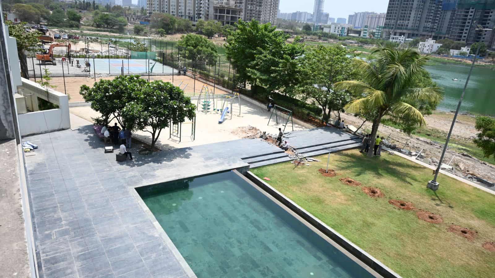 Swimming pool and green garden area in a modern residential complex with city skyline in the background.